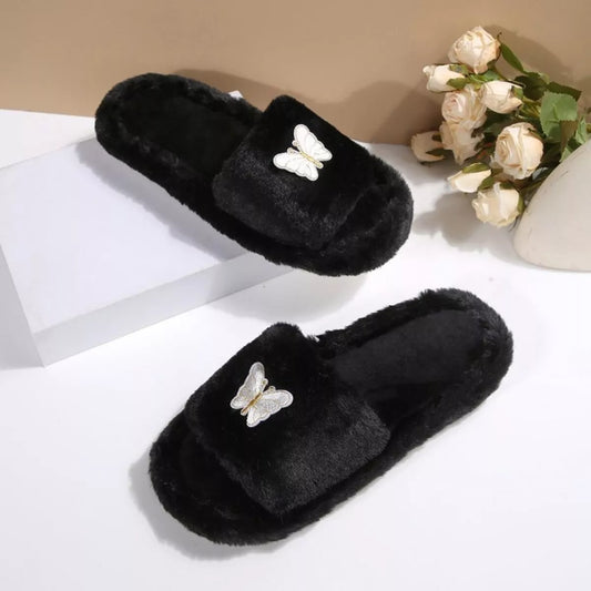 Black slippers with butterfly decorations on a white surface with flowers in the background