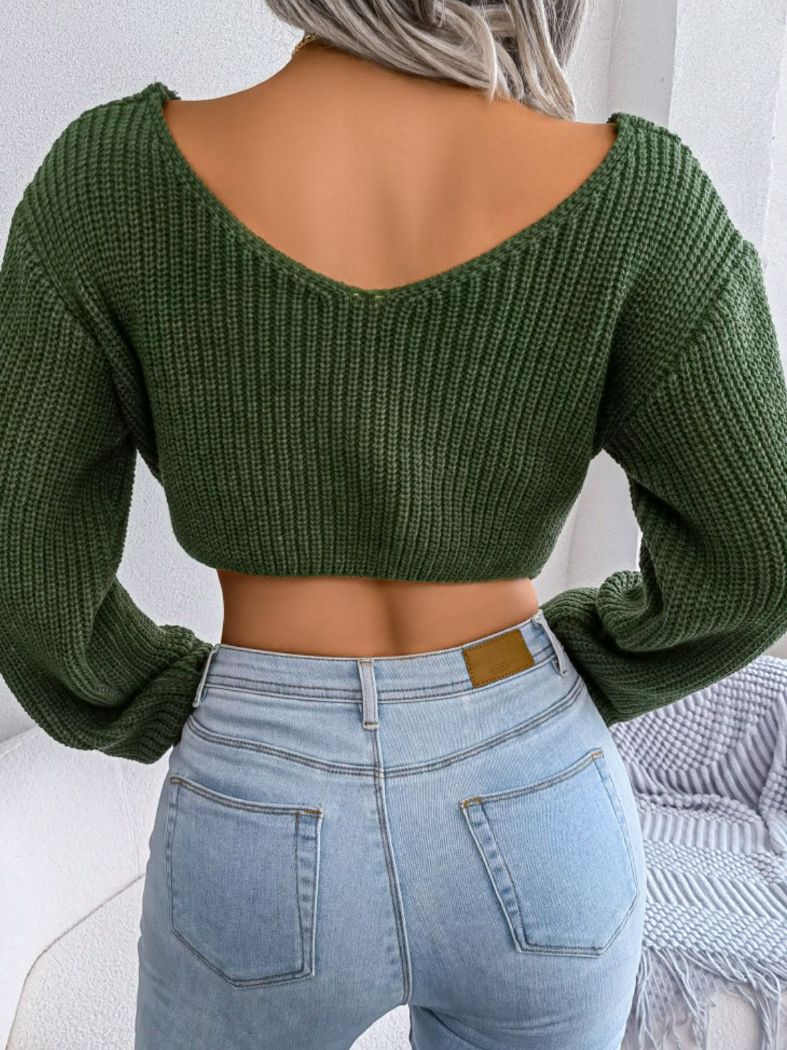 Green cropped sweater and light blue jeans worn by a person against a neutral background