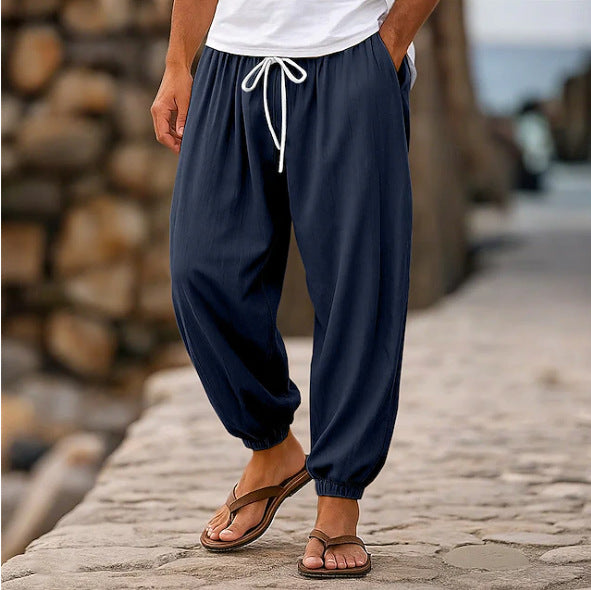Person wearing navy blue jogger pants with a white shirt and brown sandals on a stone path.