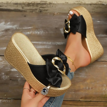 Gold platform sandals with black ribbons held by a hand on a wooden floor.