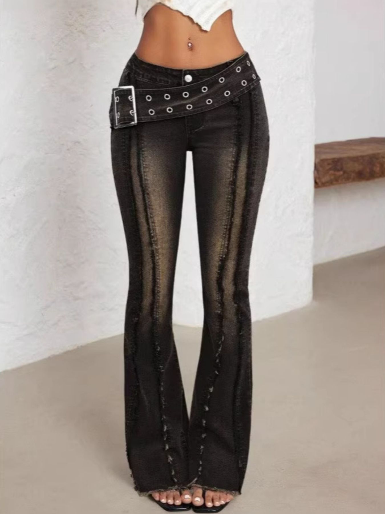 Black flared jeans with a belt on a plain background