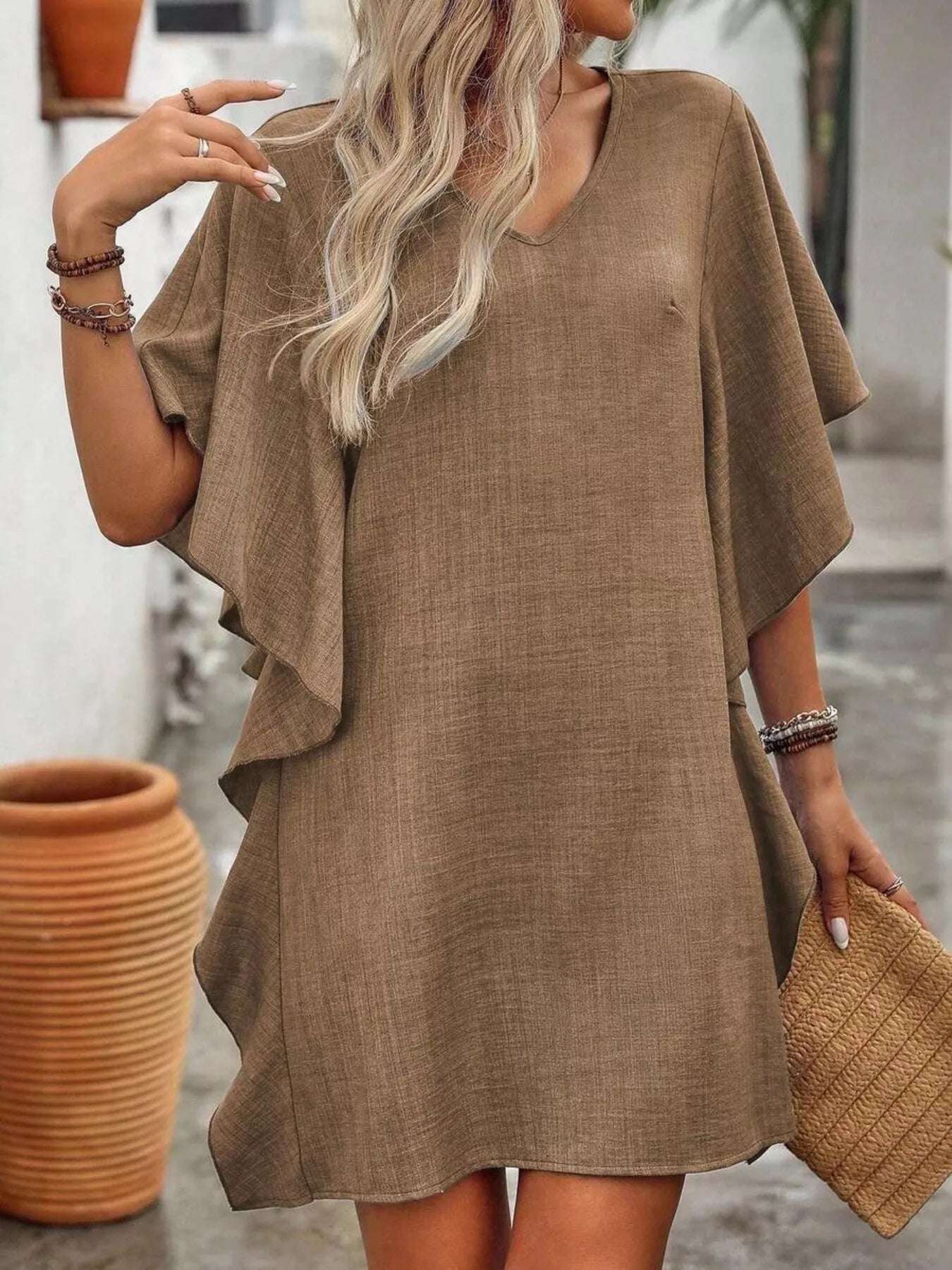 Woman wearing a brown dress holding a matching clutch outdoors.