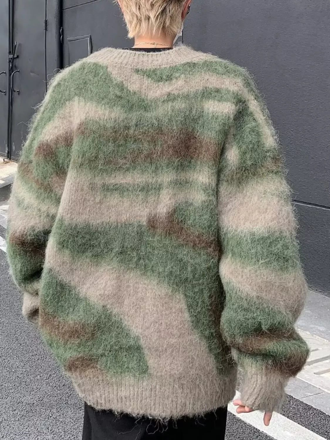 Person wearing a green and beige patterned sweater with a neutral background