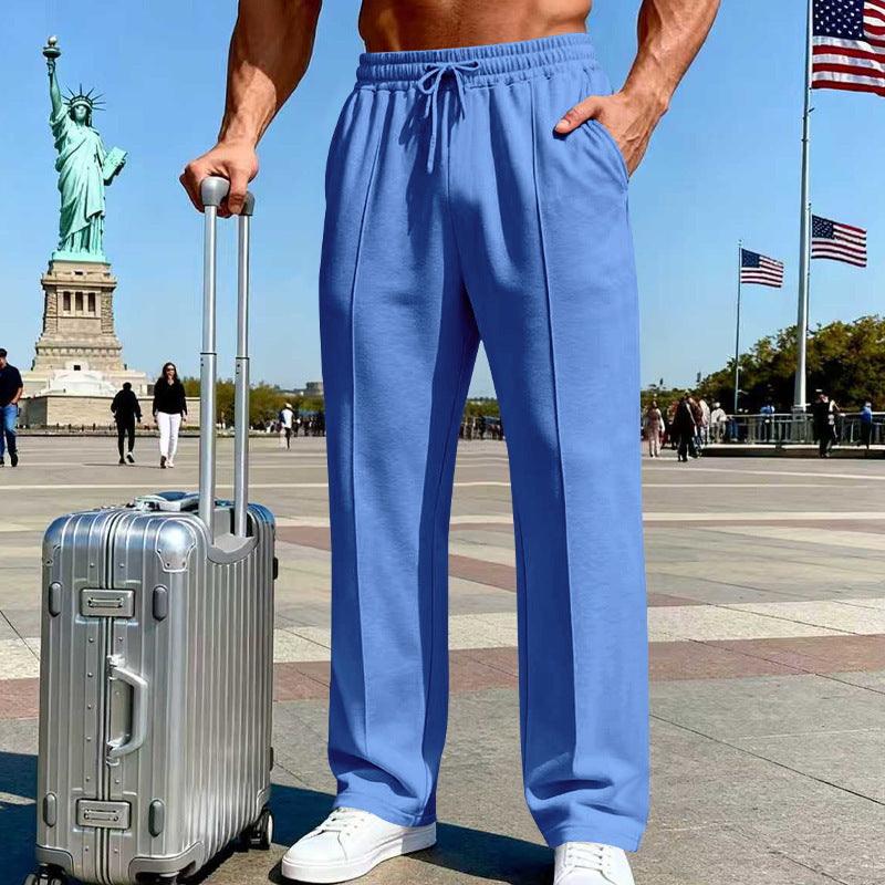 Person wearing blue pants standing with a silver suitcase in front of the Statue of Liberty and American flags.