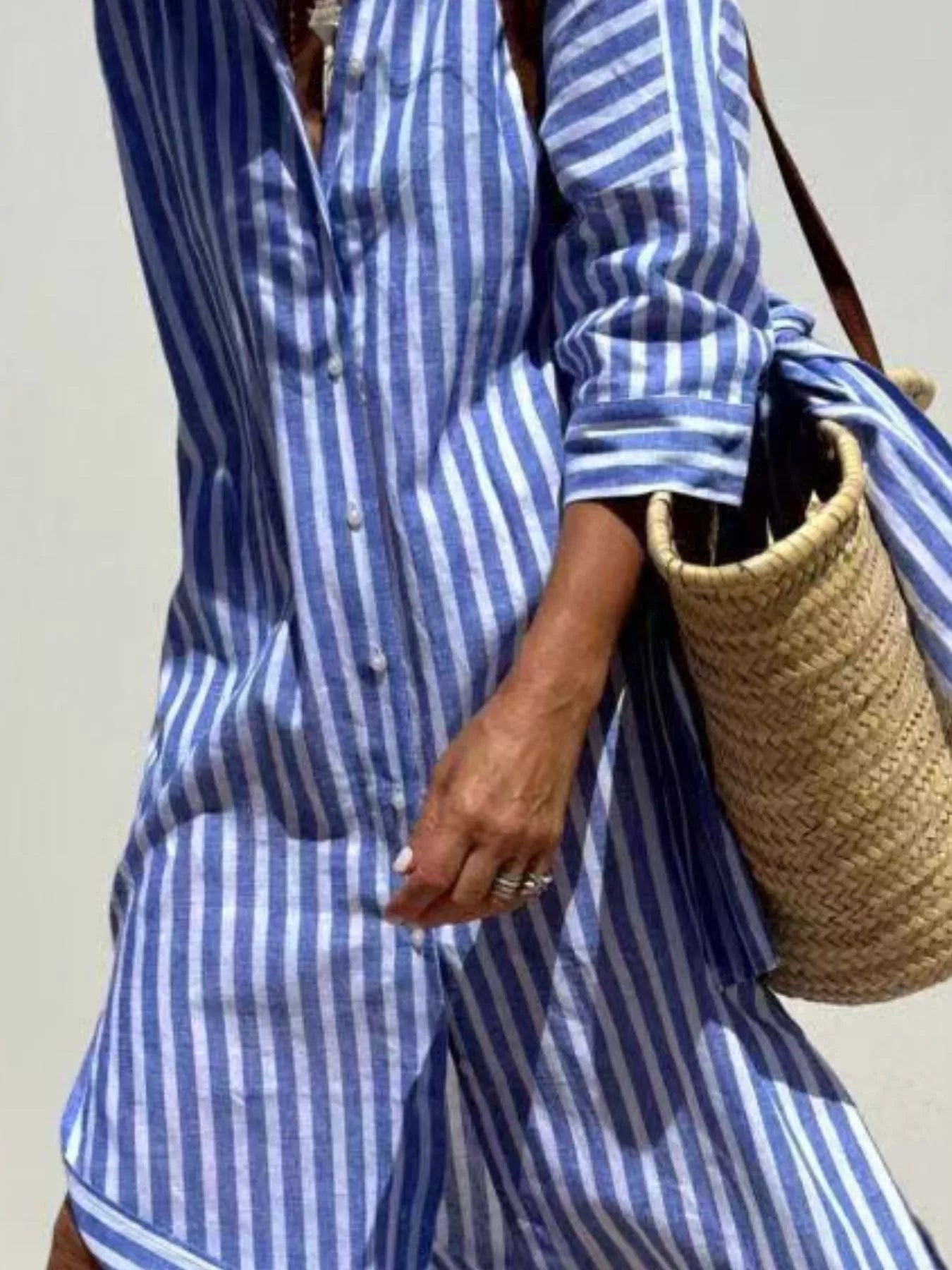 Person wearing a blue and white striped outfit holding a woven bag.