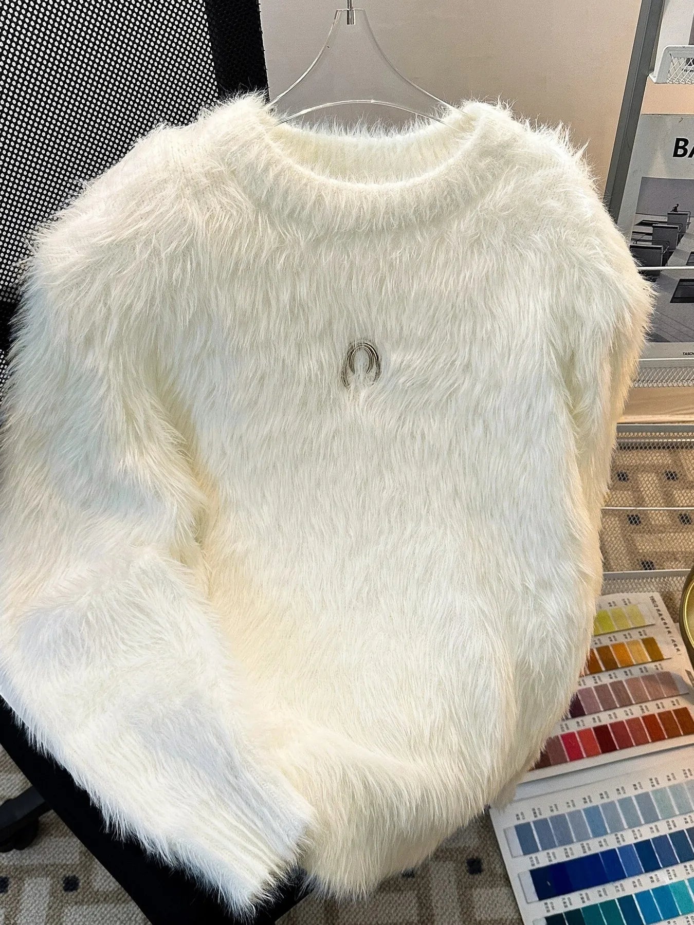 White fluffy sweater with a brand logo on a hanger against a neutral background