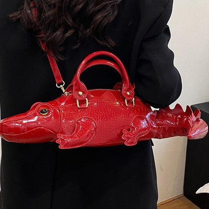 Red alligator-shaped handbag held by a person wearing a black outfit.
