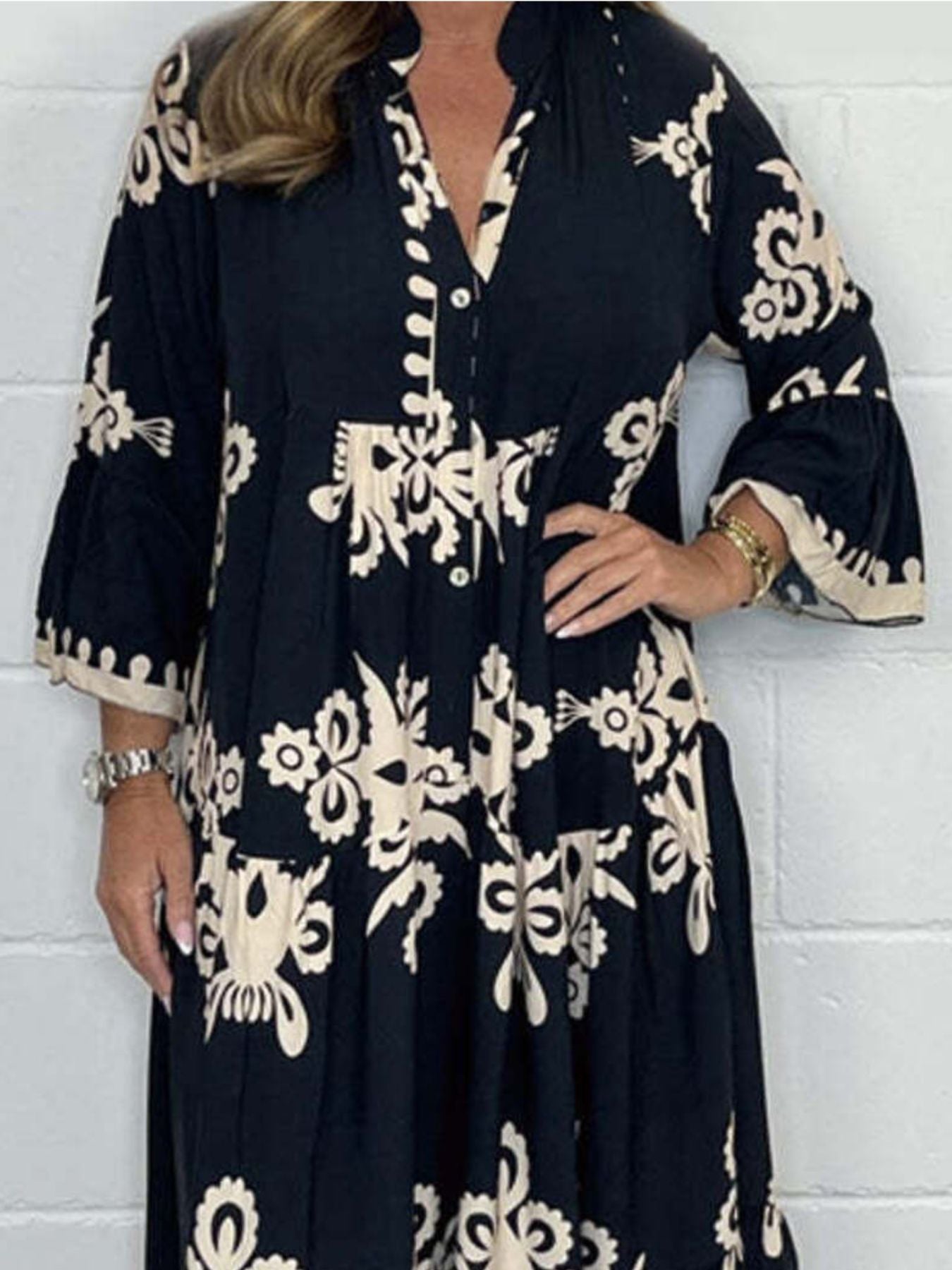 Woman wearing a black dress with white floral patterns against a white tiled wall.