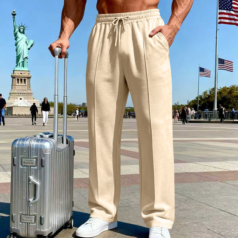 Person wearing beige sweatpants with a silver suitcase in front of the Statue of Liberty and American flags.