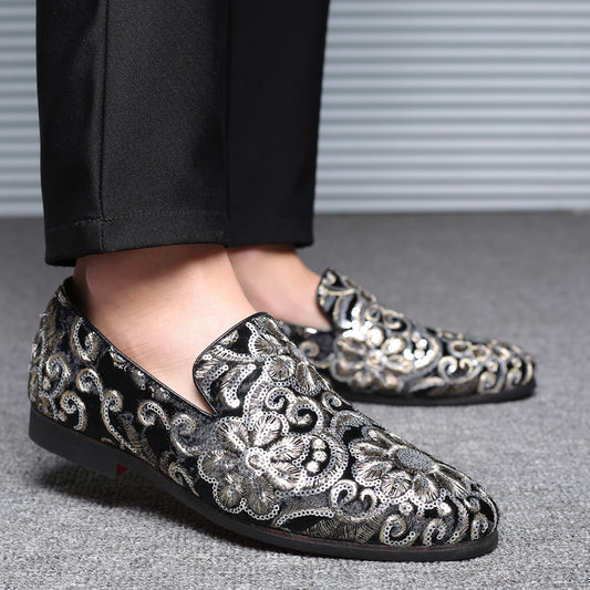 Black loafers with silver floral embroidery worn with black pants on a gray floor.