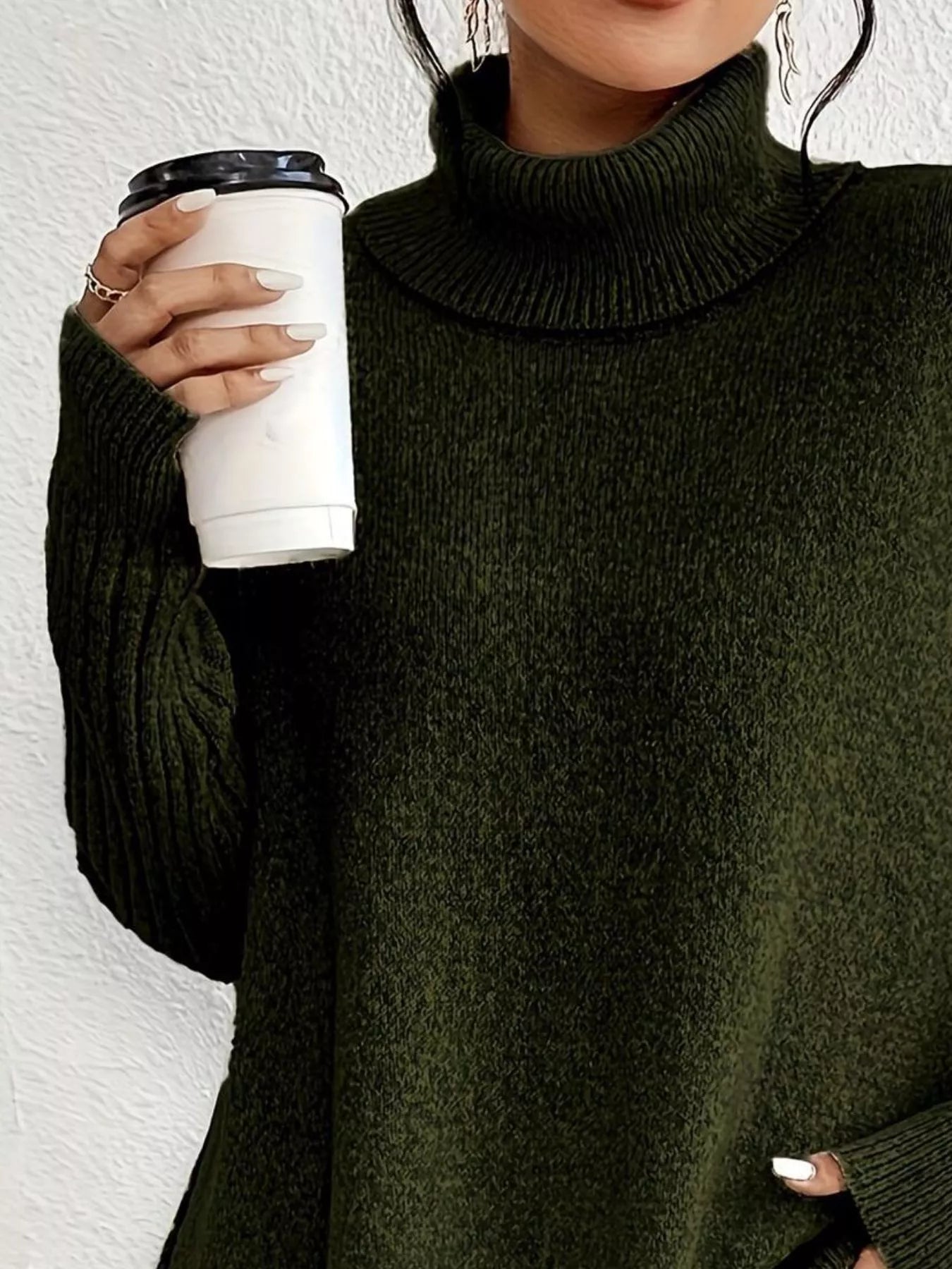 Person wearing a dark green sweater holding a white coffee cup against a white background