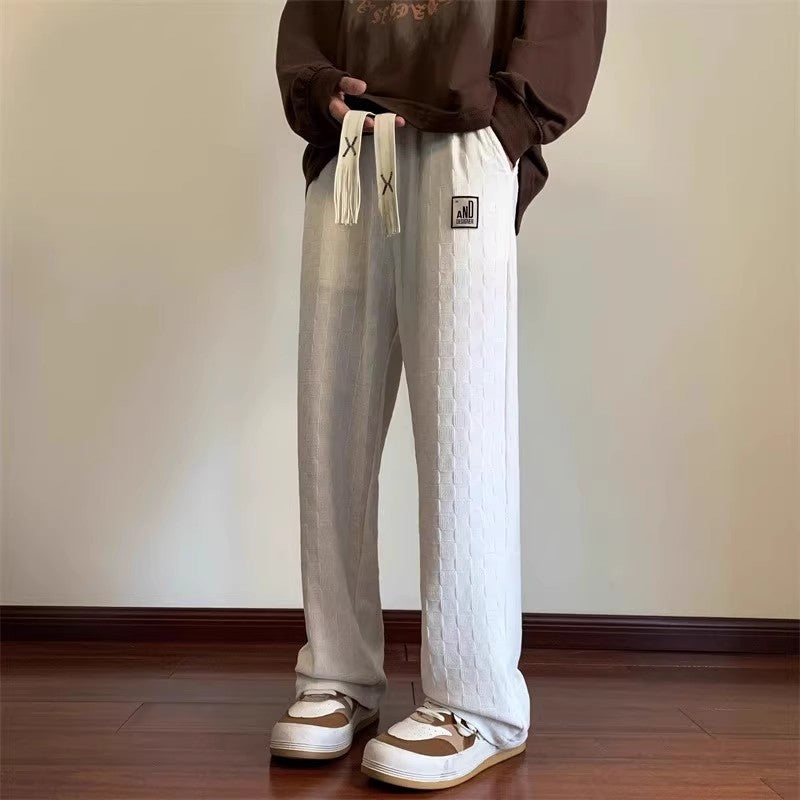 Person wearing white textured pants with a brown sweatshirt and shoes in a room.