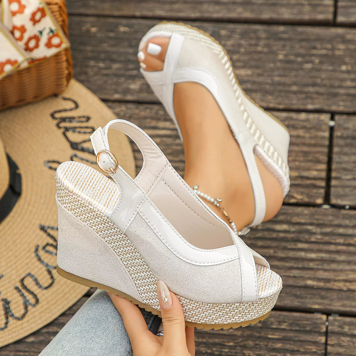 White wedge sandals with woven sole held by a hand on a wooden floor.