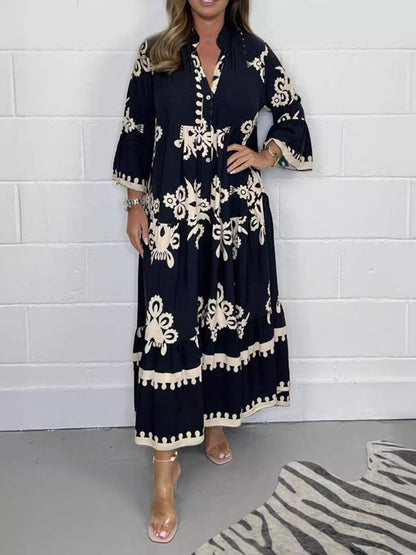 Woman wearing a black dress with white patterns against a white brick wall.