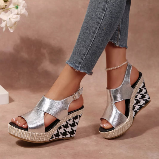 Silver wedge sandals with houndstooth pattern worn by a person, with a blurred floral 