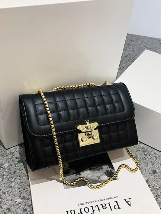 Black quilted handbag with gold chain and clasp on a gray surface