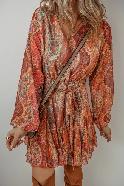 Woman wearing a patterned dress with long sleeves and a belt, standing against a plain background.
