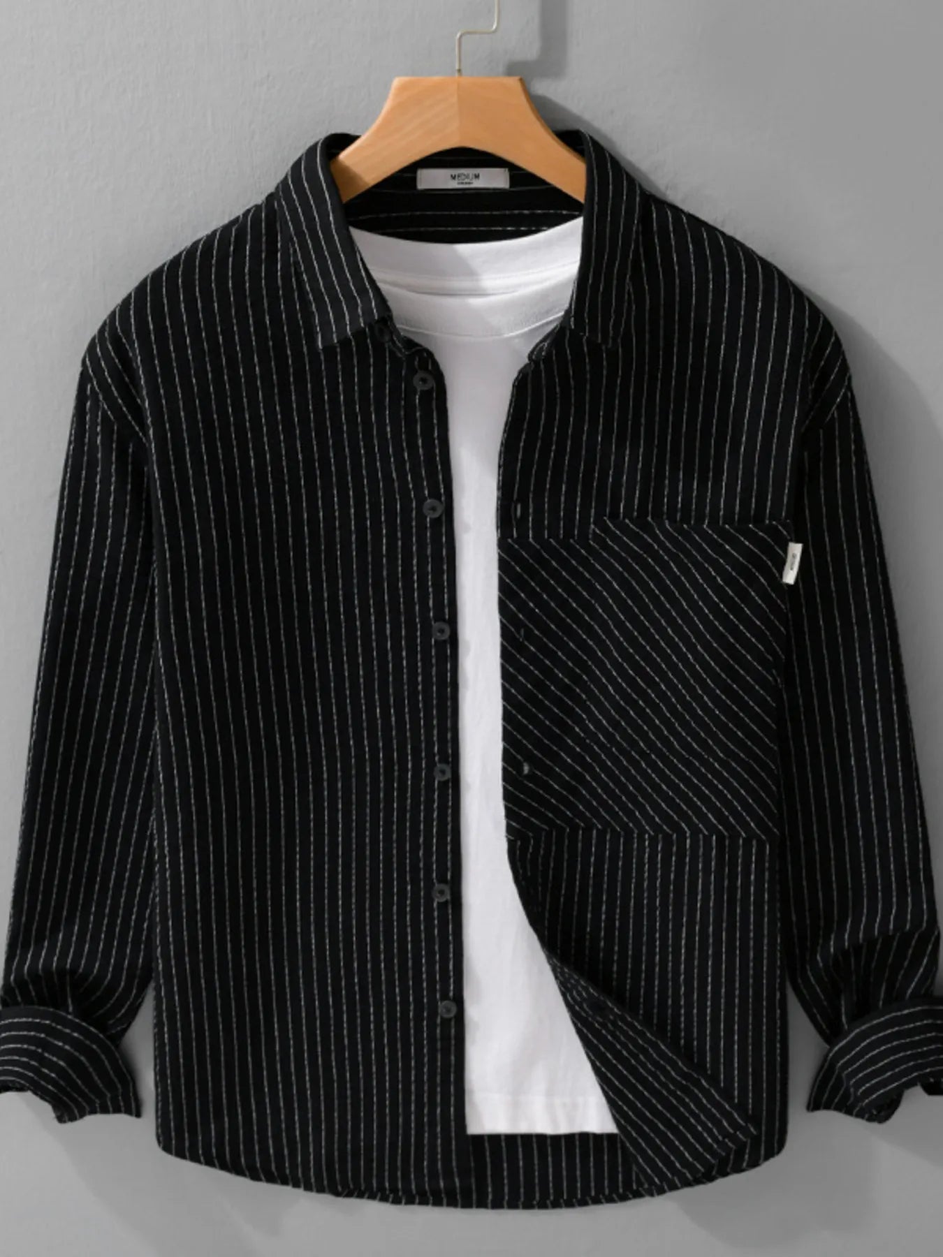 Black pinstripe shirt over a white t-shirt on a wooden hanger against a gray background