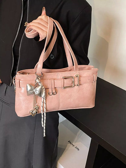 Pink handbag with decorative bow held by a person wearing a black outfit.