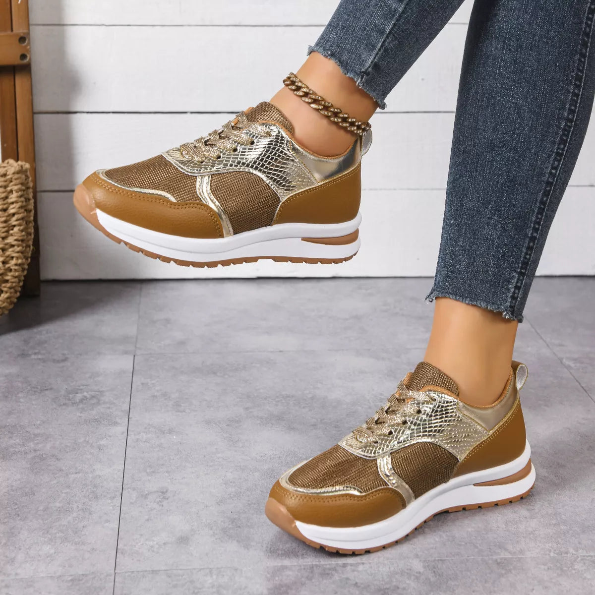 Brown and gold sneakers worn with blue jeans on a gray floor.