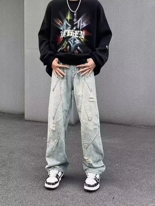 Person wearing a black sweatshirt with colorful graphics and light blue jeans against a gray background