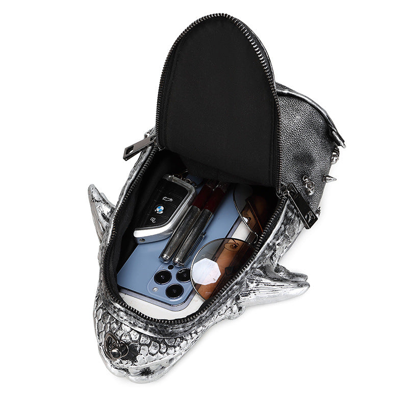 Silver shark-shaped pouch with open zipper, containing a phone and other items on a white background