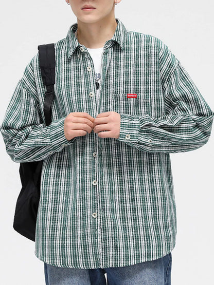 Person wearing a green plaid shirt with a small red logo, holding a black backpack.