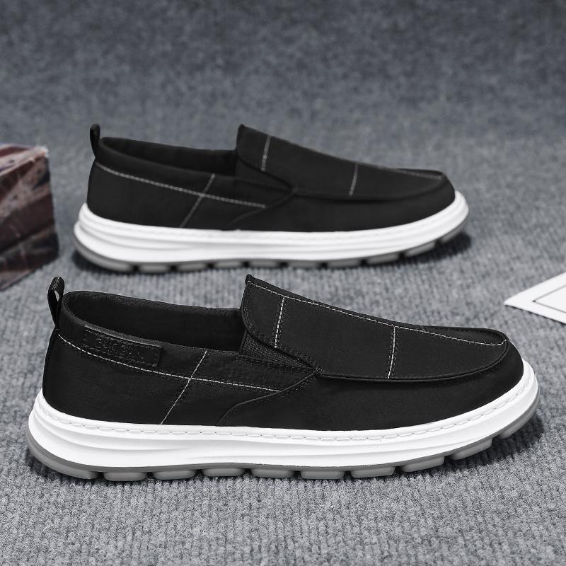 Black slip-on shoes with white soles on a gray surface