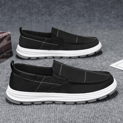 Black slip-on shoes with white soles on a gray surface