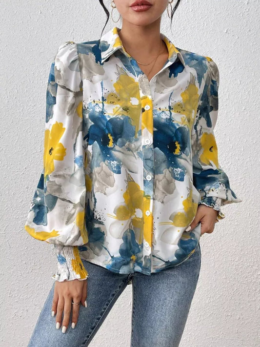 Woman wearing a floral patterned shirt with blue, yellow, and white colors against a plain background.