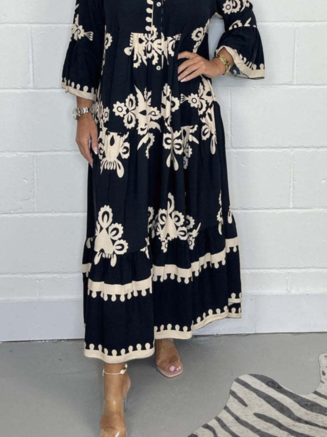 Person wearing a black dress with white floral patterns against a white brick wall.