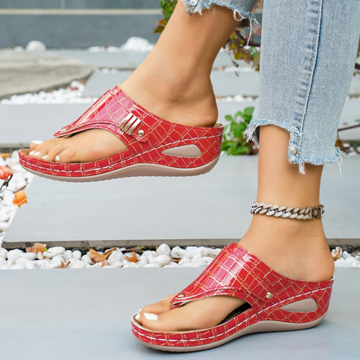 Red crocodile-patterned sandals worn with light blue jeans on a blurred outdoor background.
