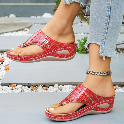 Red crocodile-patterned sandals worn with light blue jeans on a blurred outdoor background.