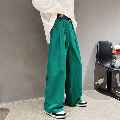 Person wearing green wide-leg pants and a white top against a gray wall.