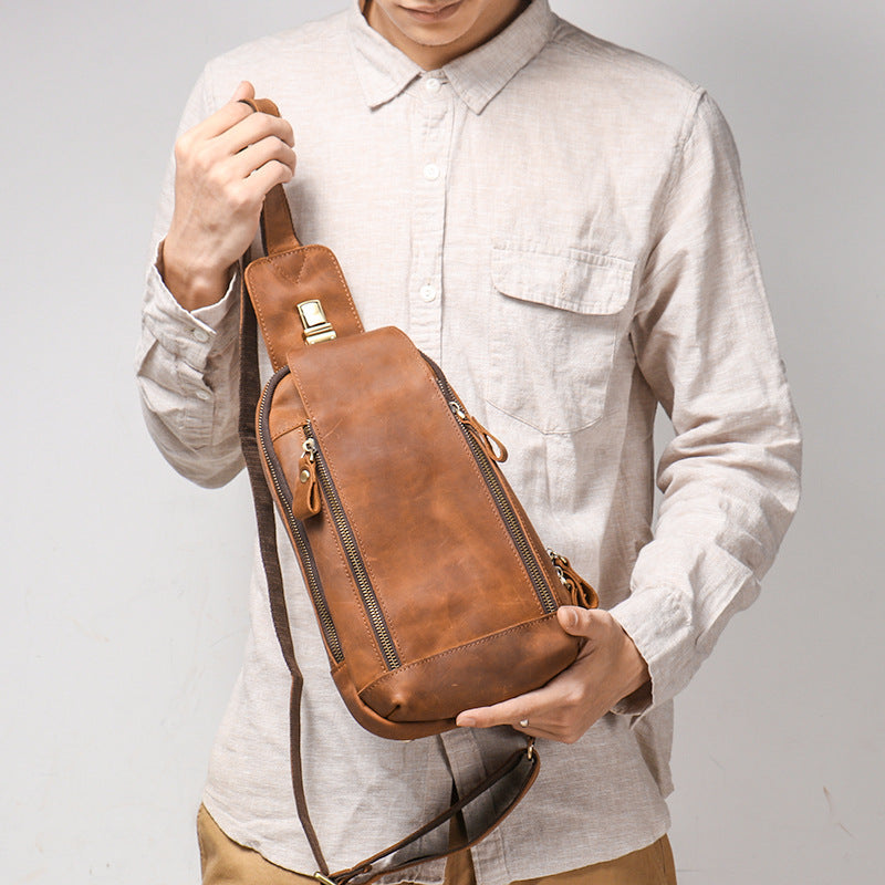 Person holding a brown leather sling bag against a plain background