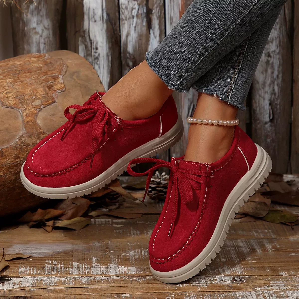 Red suede shoes with white soles worn by a person on a wooden surface.