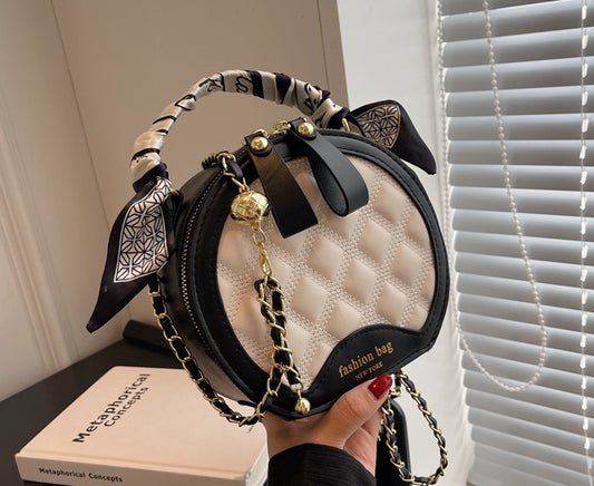Black and white quilted handbag with decorative elements held by a person, placed on a surface with a book in the background.