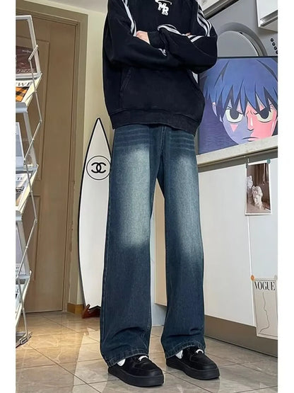 Person wearing a black hoodie and blue jeans standing in a room with posters on the wall.