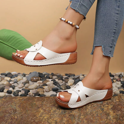 White sandals with brown soles worn by a person on a stone surface.