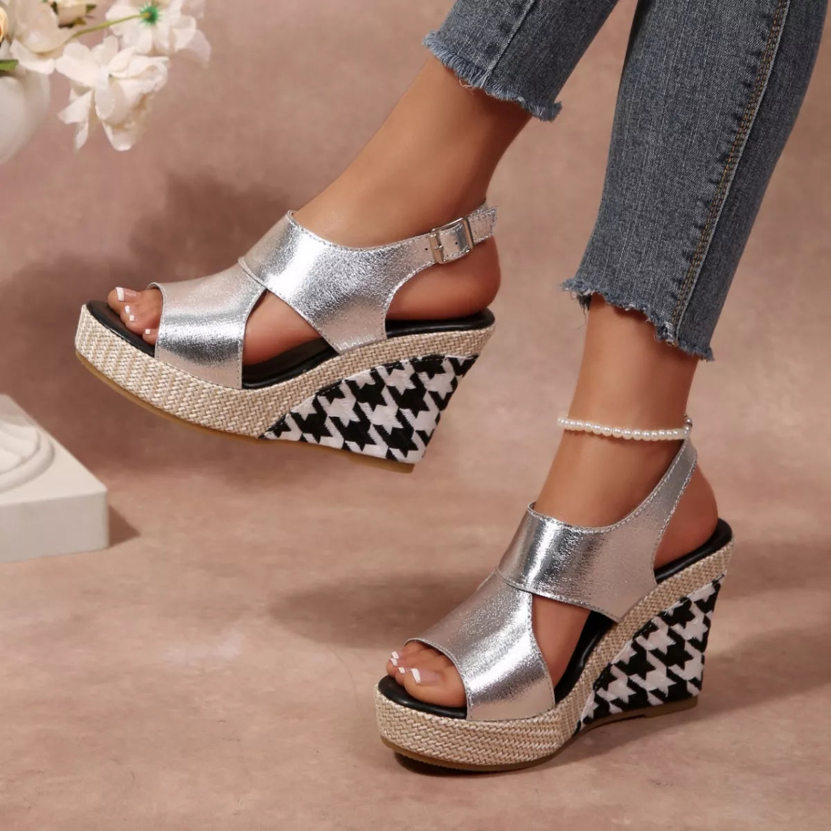 Silver wedge sandals with houndstooth pattern worn by a person, with a blurred floral 