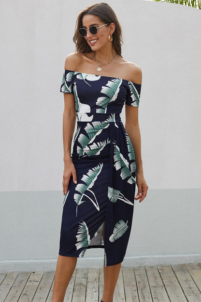 Woman wearing a navy off-shoulder dress with tropical leaf pattern against a light gray wall.