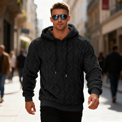 Man wearing a dark gray cable knit hoodie and sunglasses walking on a city street.