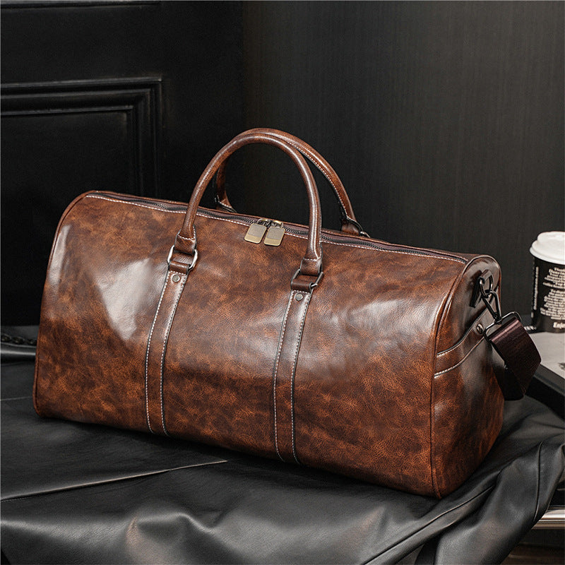 Brown leather duffel bag on a black surface with a dark background
