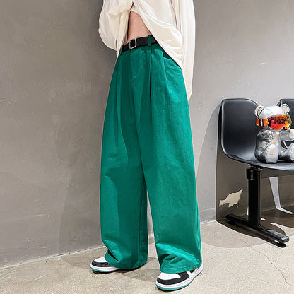 Person wearing teal pants and a white shirt against a gray wall with a chair and stuffed animals in the background.