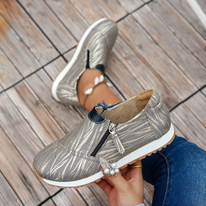 Person holding a patterned shoe with a zipper on a wooden floor.