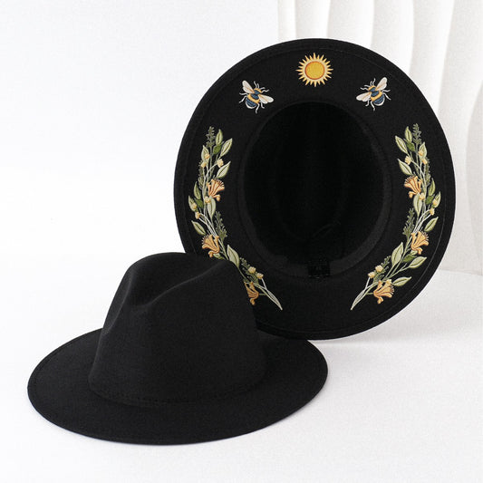 Black hat with floral and bee embroidery on a white background