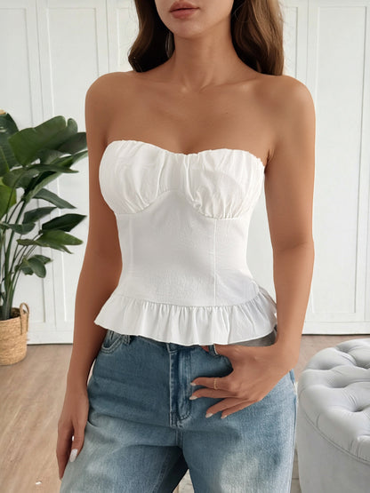Woman wearing a white strapless top and blue jeans in a room with a plant and gray ottoman.