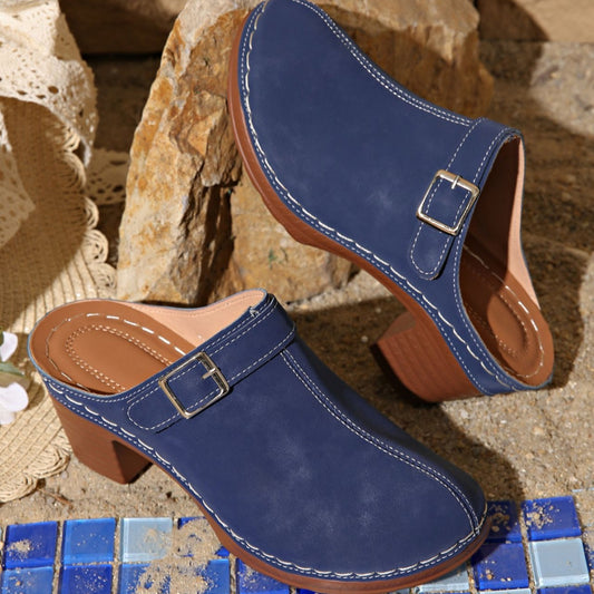 Pair of blue clogs with brown soles on a stone surface