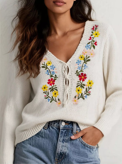 White sweater with colorful floral embroidery worn by a person against a neutral background