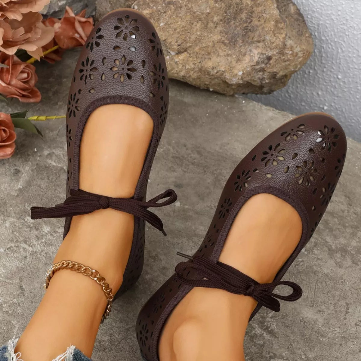 Brown perforated shoes with lace-up design worn by a person on a stone surface.